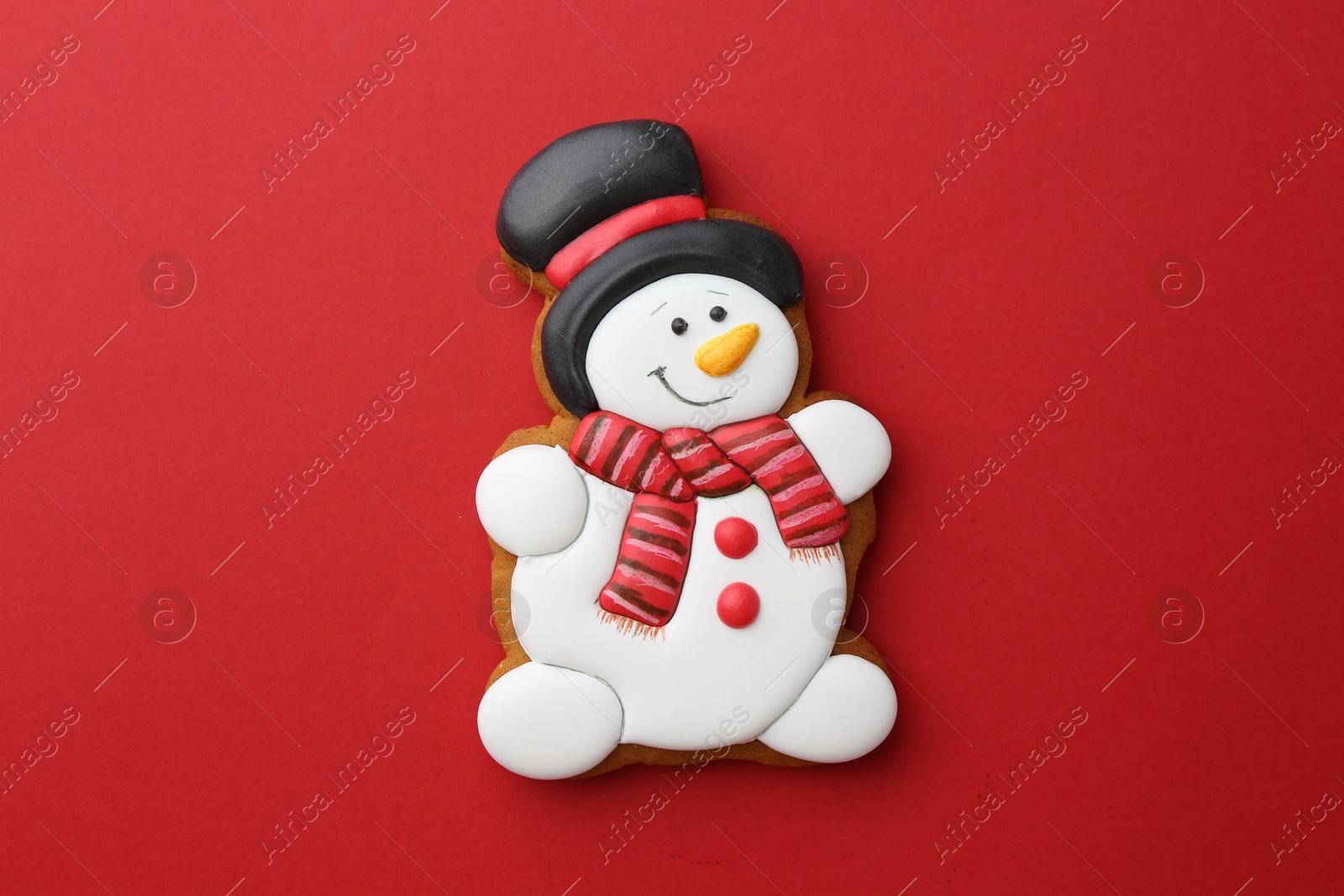 Photo of Tasty Christmas cookie in shape of snowman on red background, top view