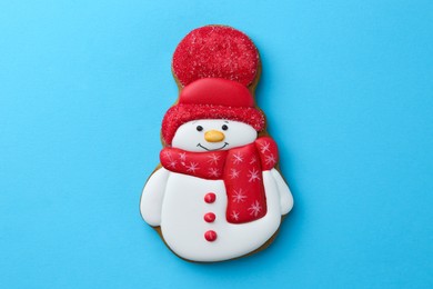 Photo of Tasty Christmas cookie in shape of snowman on light blue background, top view