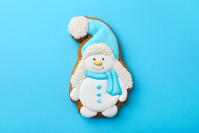 Photo of Tasty Christmas cookie in shape of snowman on light blue background, top view