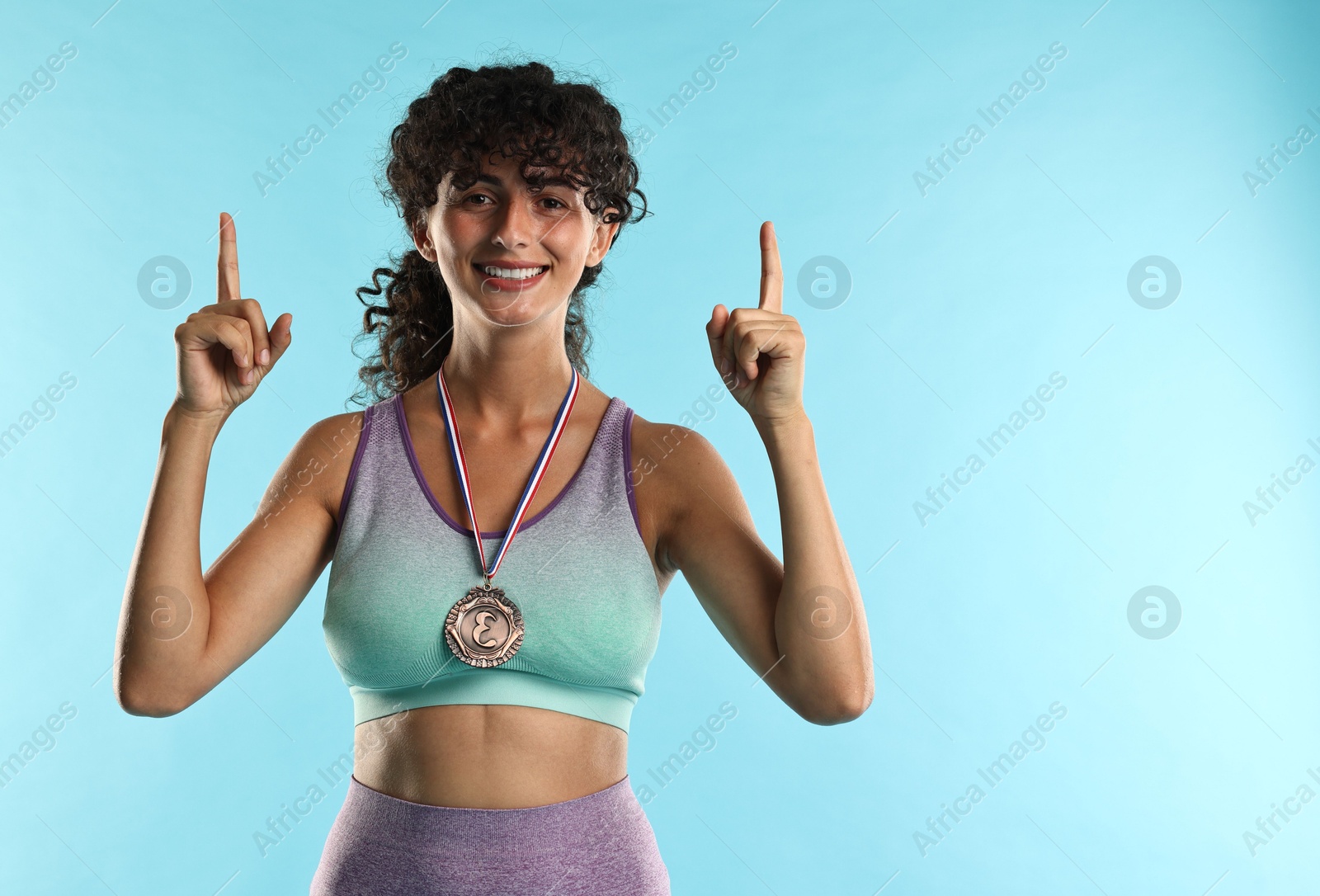 Photo of Happy winner with bronze medal pointing upwards on light blue background. Space for text