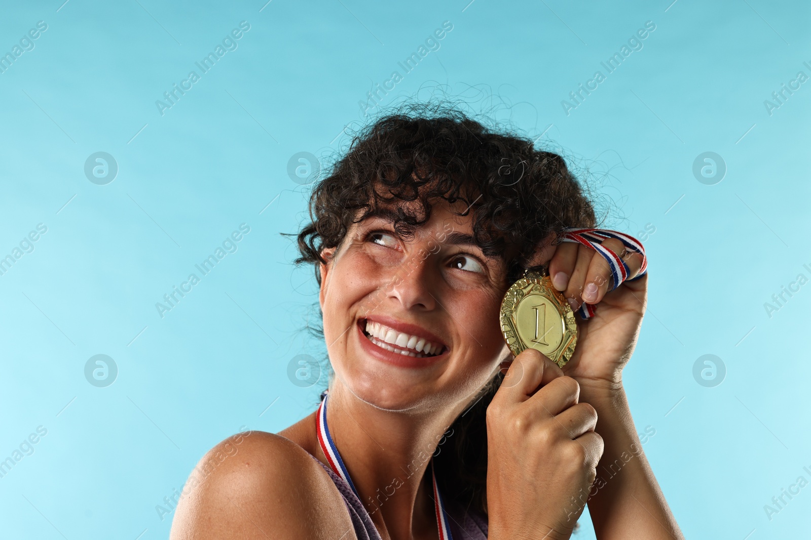 Photo of Happy winner with golden medal on light blue background, closeup