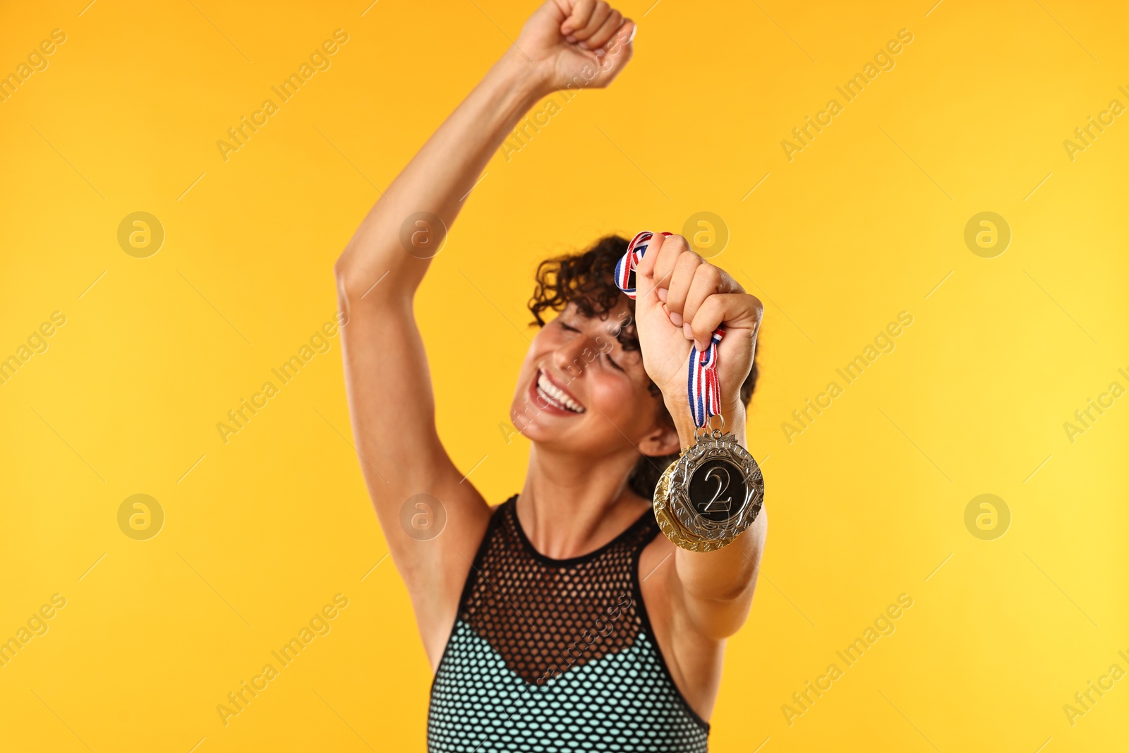 Photo of Happy winner showing different medals on yellow background, selective focus