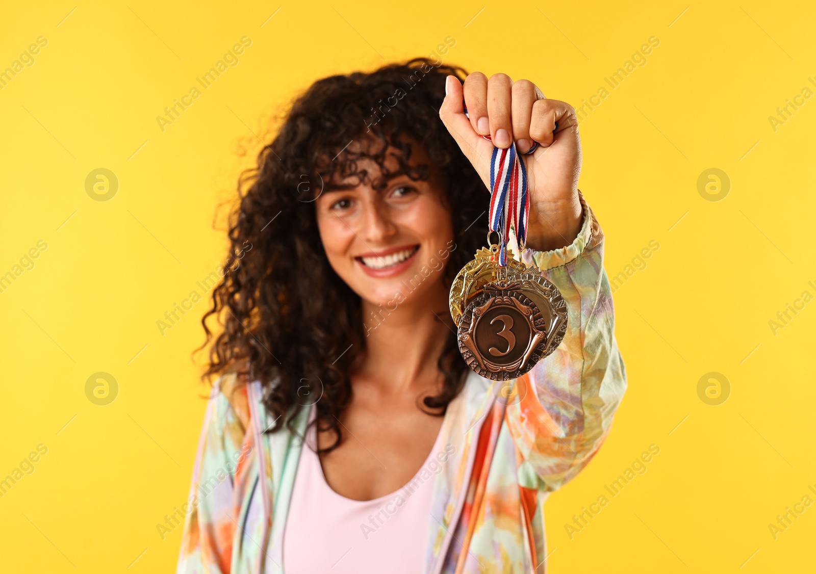 Photo of Happy winner showing different medals on yellow background, selective focus