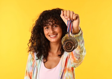 Happy winner showing different medals on yellow background, selective focus