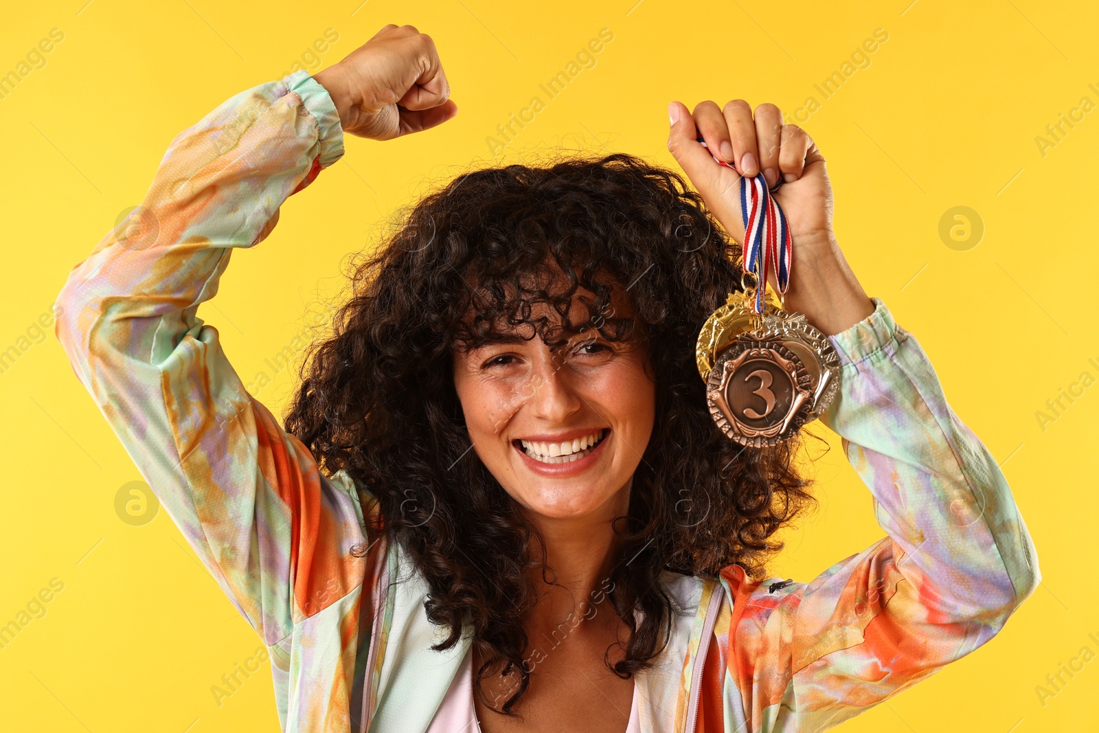 Photo of Happy winner showing different medals on yellow background