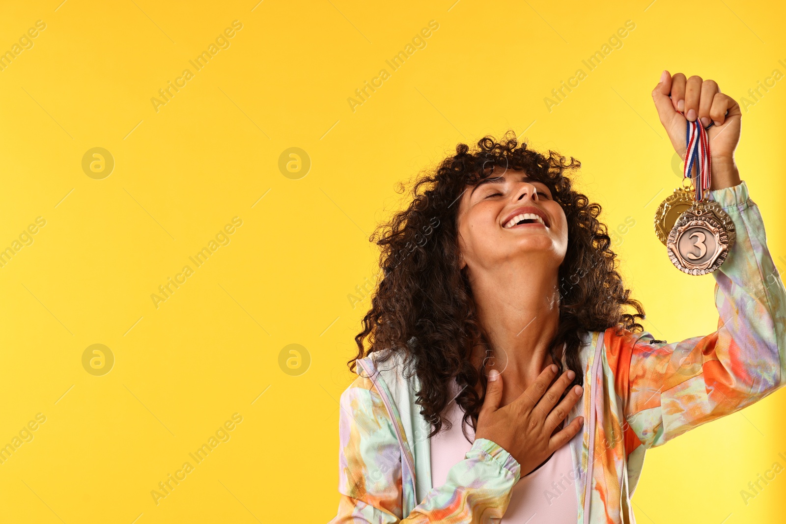 Photo of Happy winner showing different medals on yellow background. Space for text