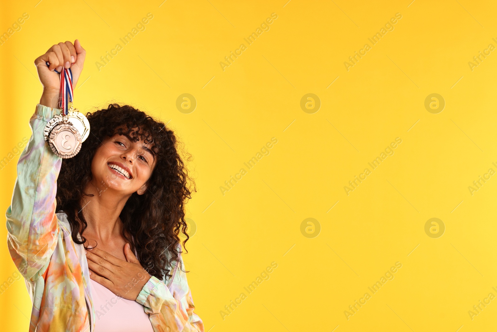 Photo of Happy winner showing different medals on yellow background. Space for text