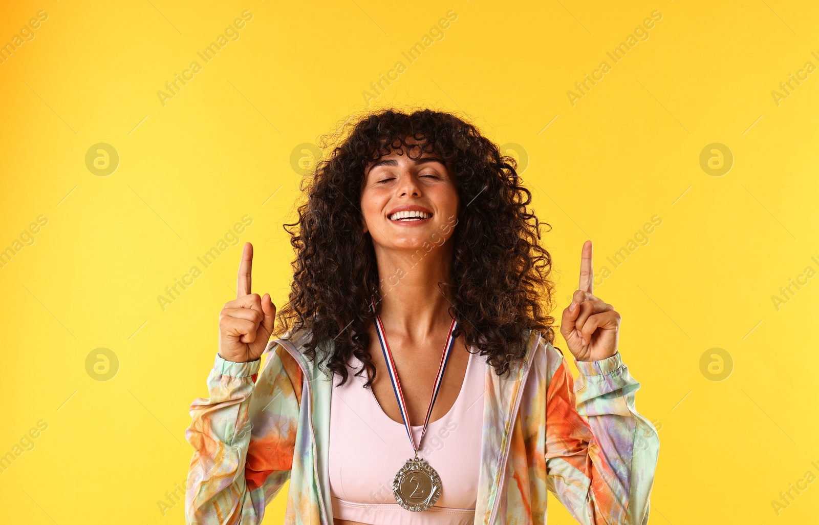 Photo of Happy winner with silver medal pointing upwards on yellow background