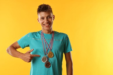 Happy winner pointing at his medals on yellow background. Space for text