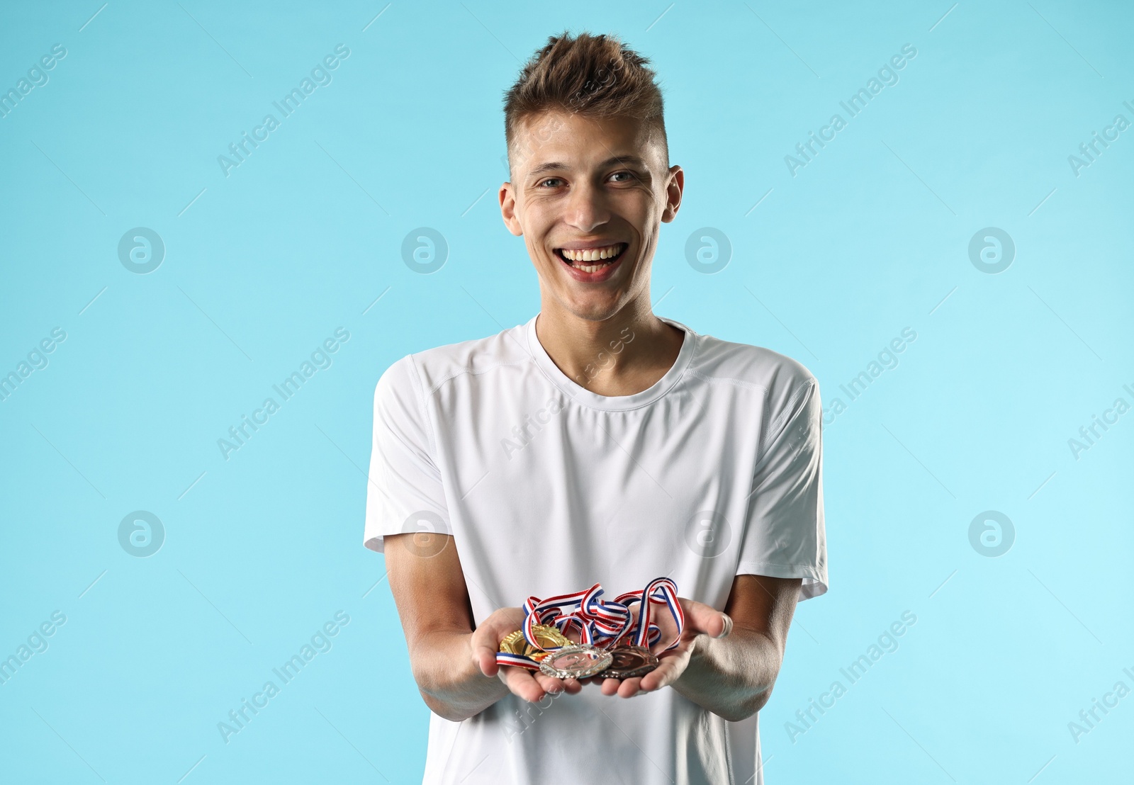 Photo of Happy winner with different medals on light blue background