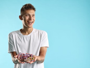 Photo of Happy winner with different medals on light blue background. Space for text