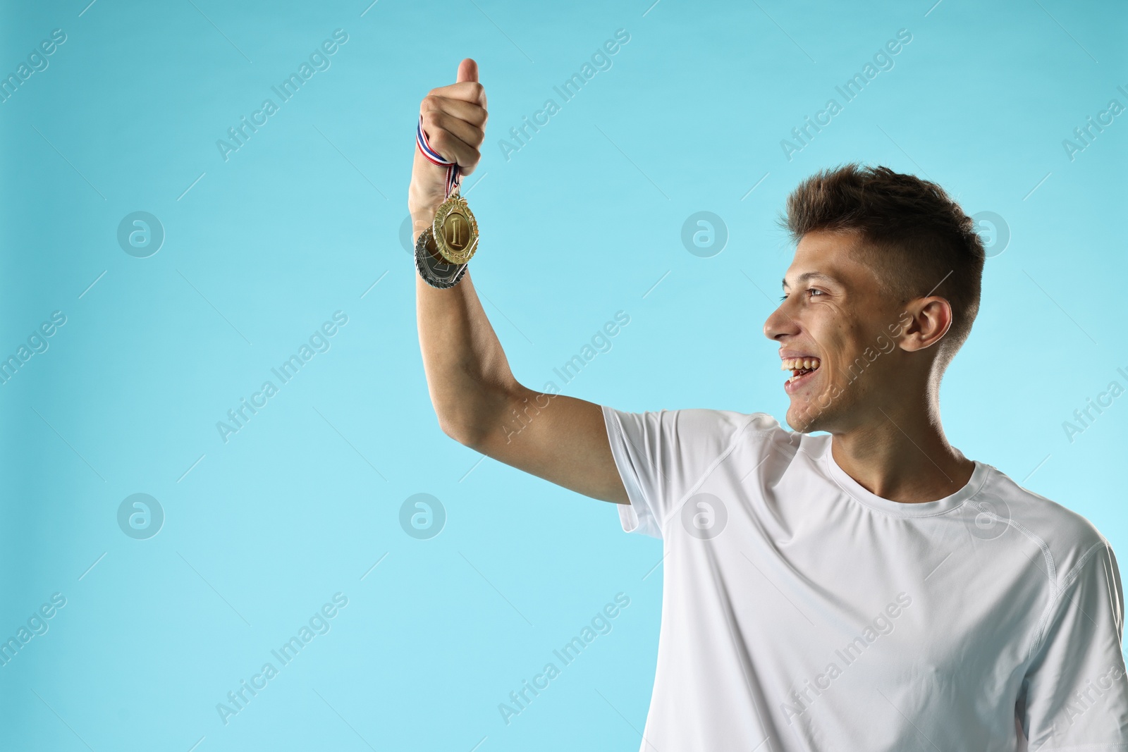 Photo of Happy winner with different medals on light blue background. Space for text