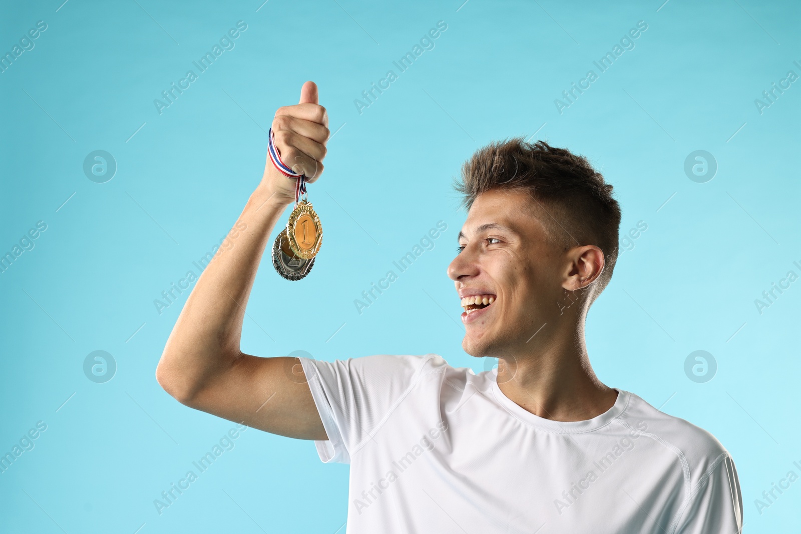 Photo of Happy winner with different medals on light blue background