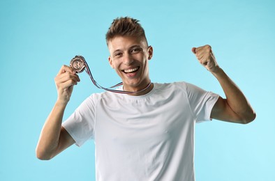 Photo of Happy winner with bronze medal on light blue background