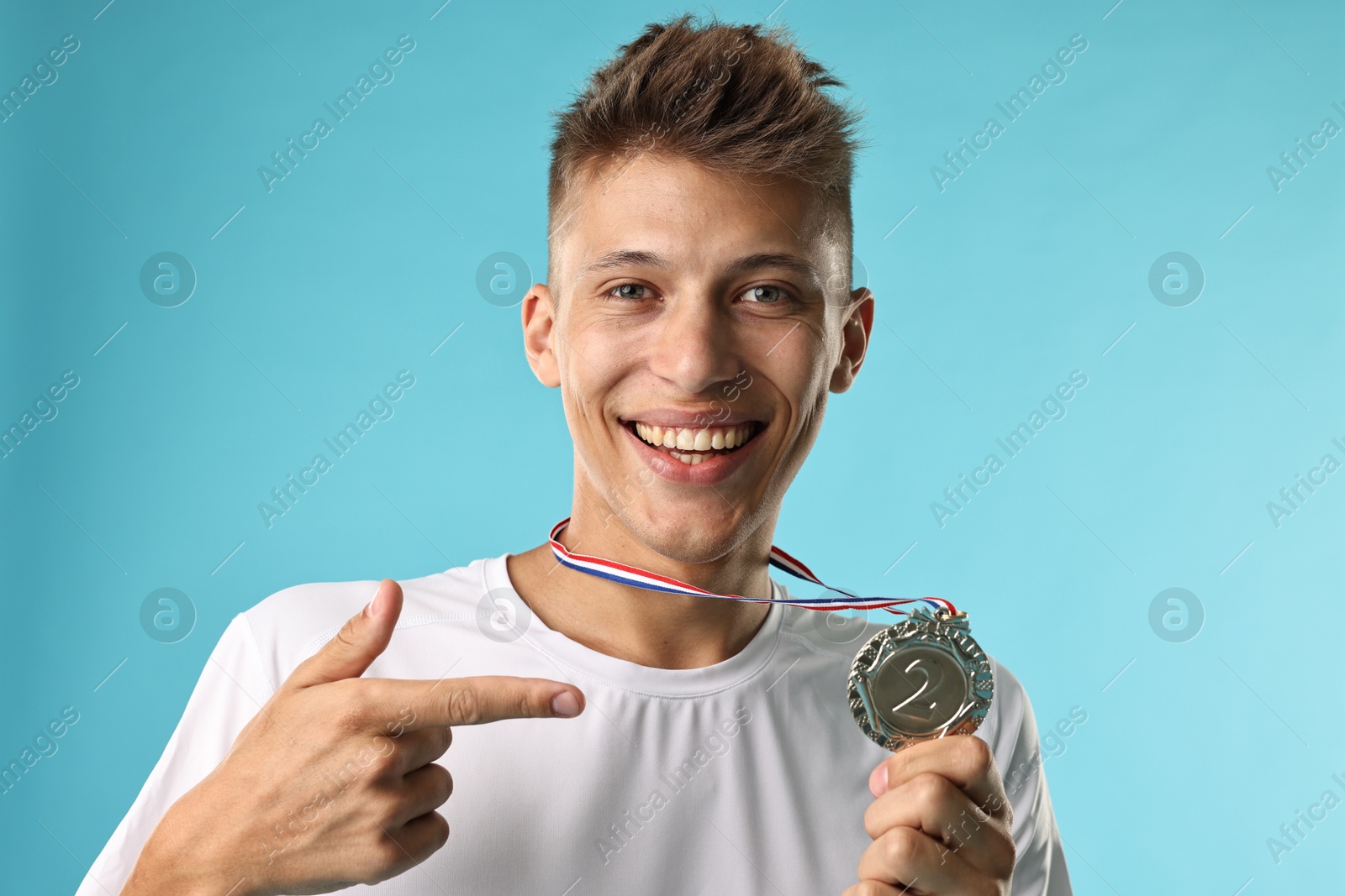 Photo of Happy winner pointing at his silver medal on light blue background