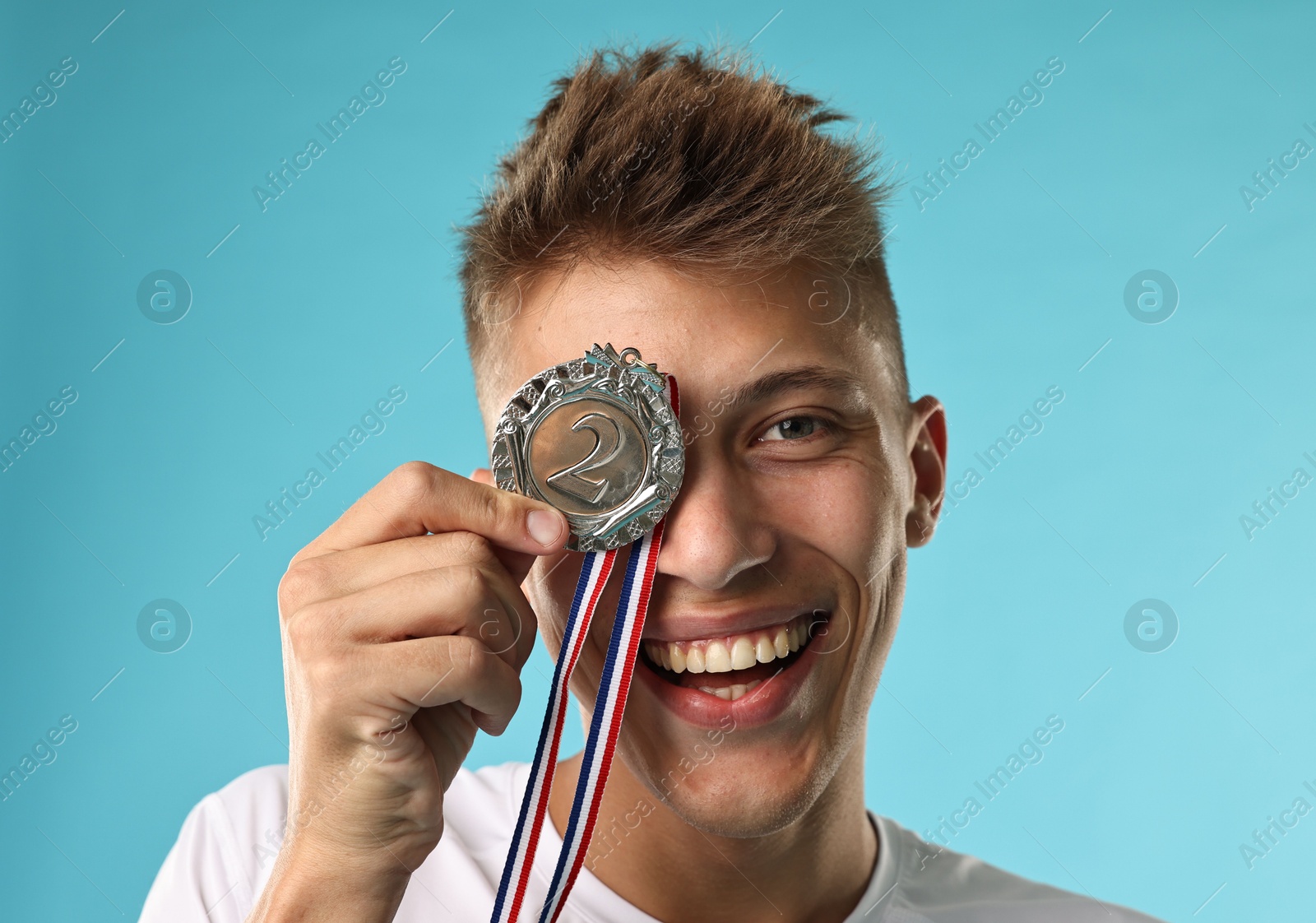 Photo of Happy winner with silver medal on light blue background, closeup