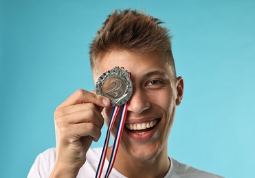 Photo of Happy winner with silver medal on light blue background, closeup