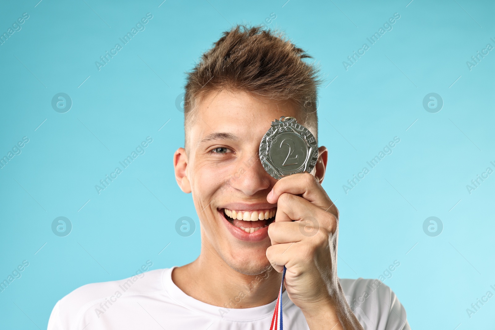 Photo of Happy winner with silver medal on light blue background, closeup