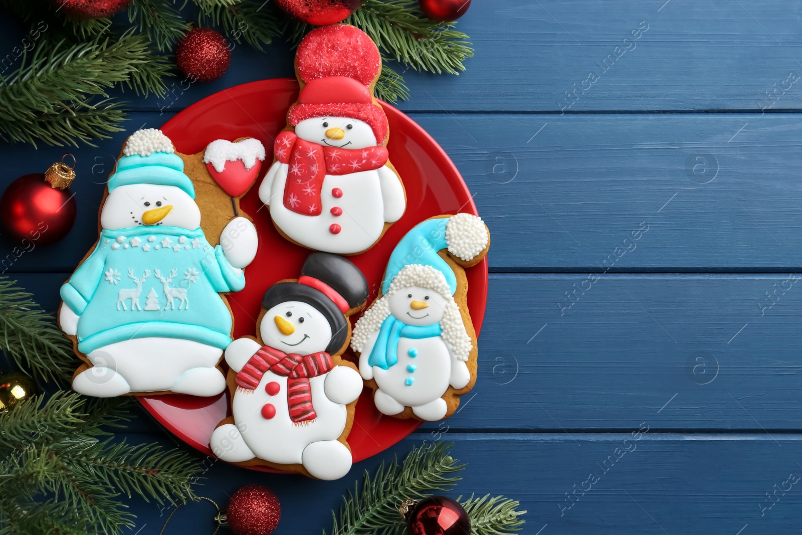 Photo of Delicious cookies in shape of snowmen and Christmas decor on blue wooden table, flat lay. Space for text