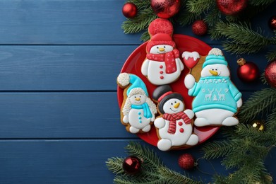 Photo of Delicious cookies in shape of snowmen and Christmas decor on blue wooden table, flat lay. Space for text