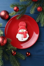 Photo of Delicious cookie in shape of snowman and Christmas decor on blue wooden table, flat lay