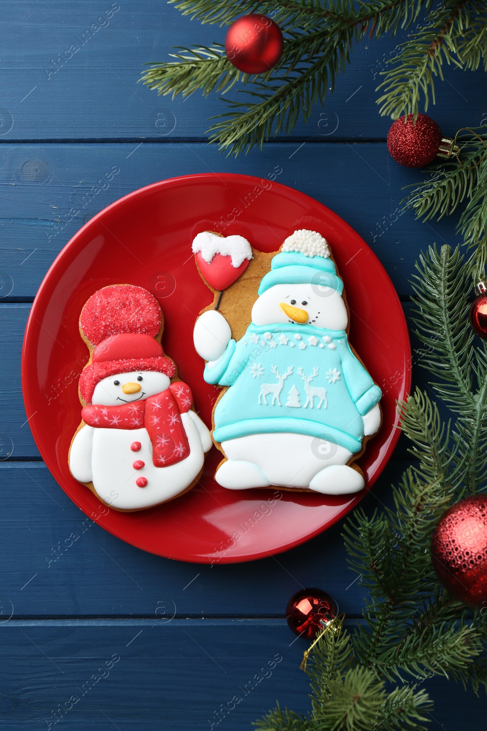 Photo of Delicious cookies in shape of snowmen and Christmas decor on blue wooden table, flat lay