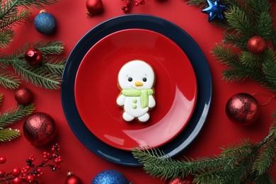 Photo of Delicious cookie in shape of snowman and Christmas decor on red table, flat lay