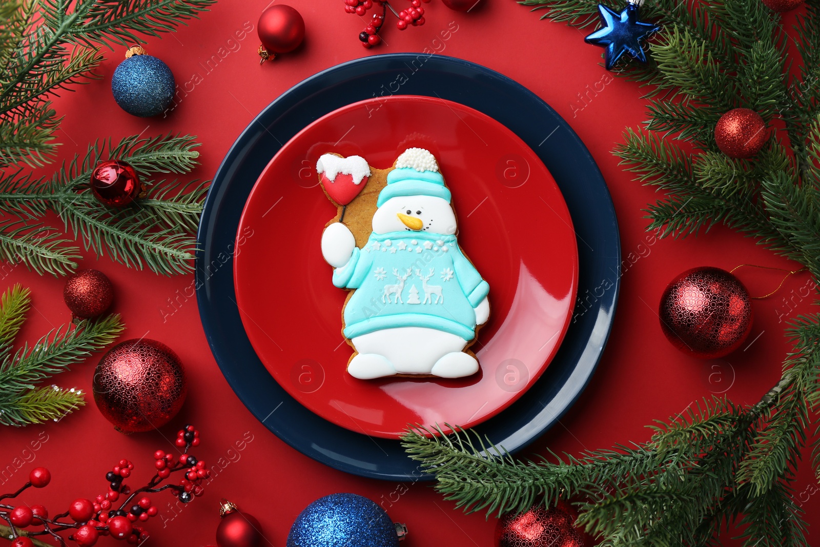 Photo of Delicious cookie in shape of snowman and Christmas decor on red table, flat lay