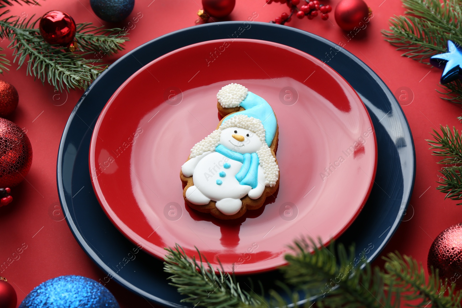 Photo of Delicious cookie in shape of snowman and Christmas decor on red table, closeup