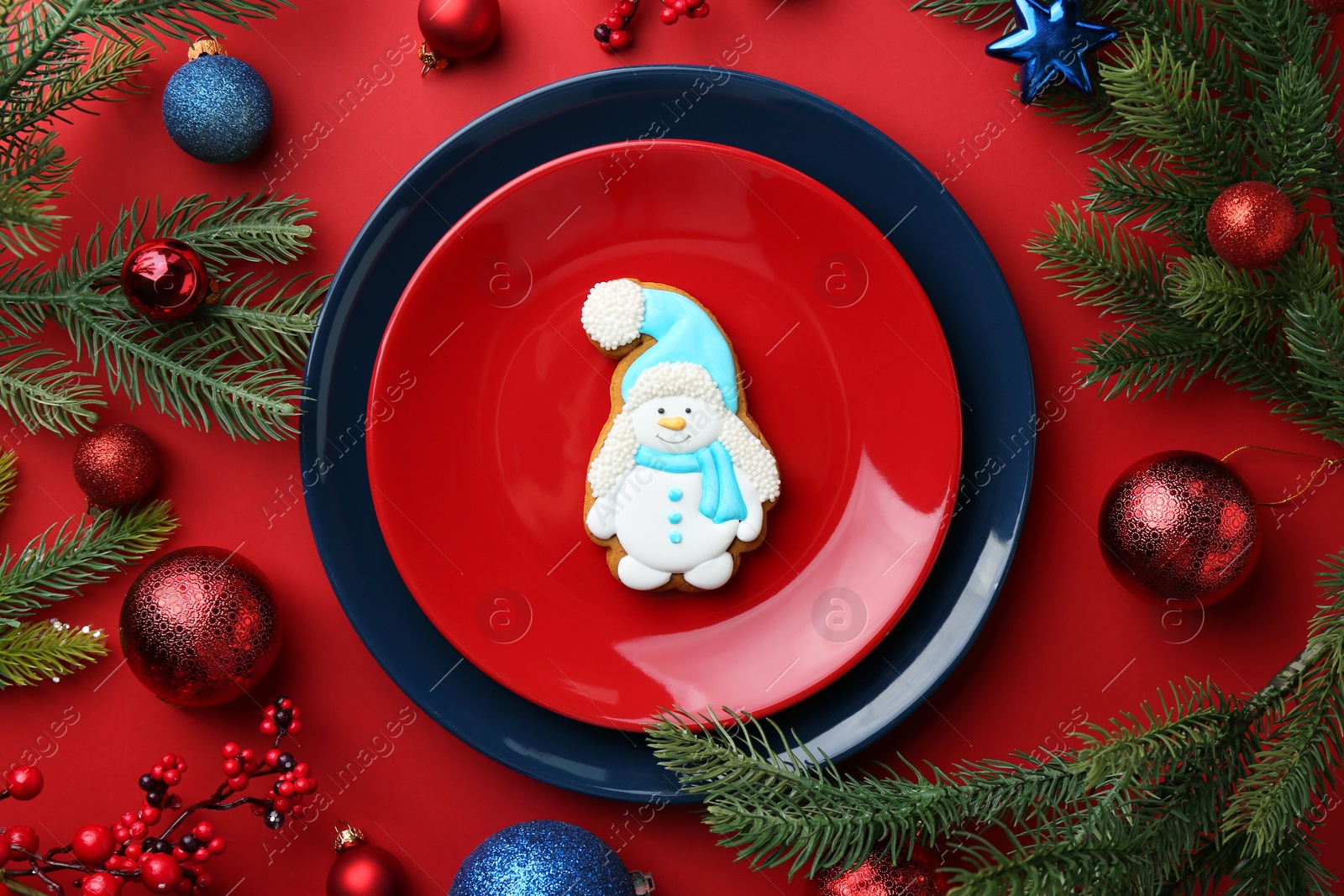 Photo of Delicious cookie in shape of snowman and Christmas decor on red table, flat lay