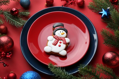 Photo of Delicious cookie in shape of snowman and Christmas decor on red table