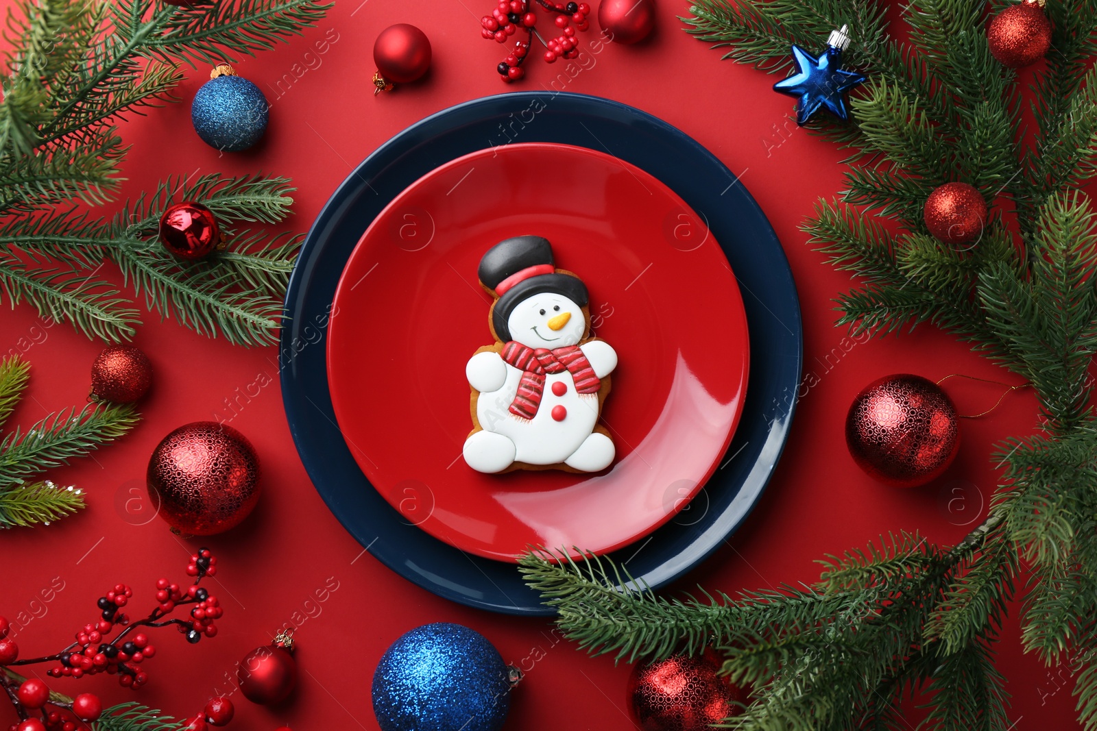 Photo of Delicious cookie in shape of snowman and Christmas decor on red table, flat lay