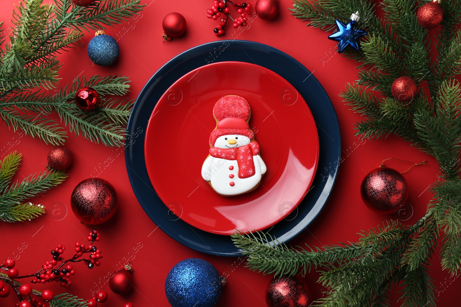 Photo of Delicious cookie in shape of snowman and Christmas decor on red table, flat lay