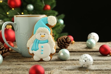 Photo of Delicious cookie in shape of snowman, cup with cocoa and Christmas decor on wooden table