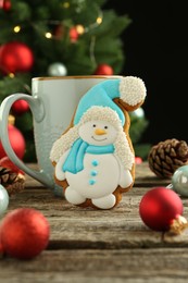 Photo of Delicious cookie in shape of snowman, cup with cocoa and Christmas decor on wooden table