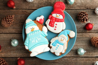 Photo of Delicious cookies in shape of snowmen and Christmas decor on wooden table, flat lay