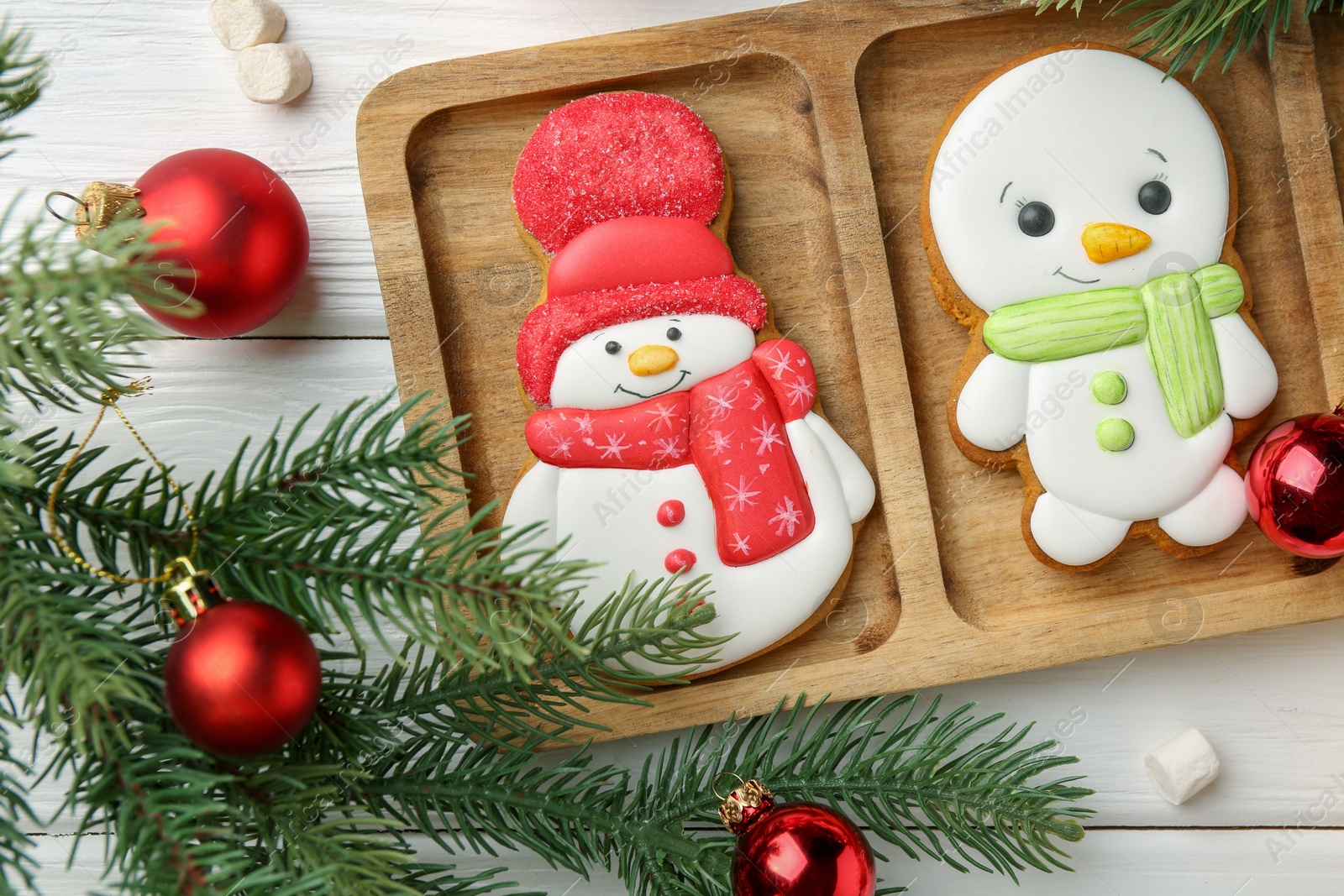 Photo of Delicious cookies in shape of snowmen, marshmallows and Christmas decor on white wooden table, flat lay