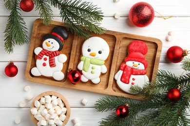 Photo of Delicious cookies in shape of snowmen, marshmallows and Christmas decor on white wooden table, flat lay