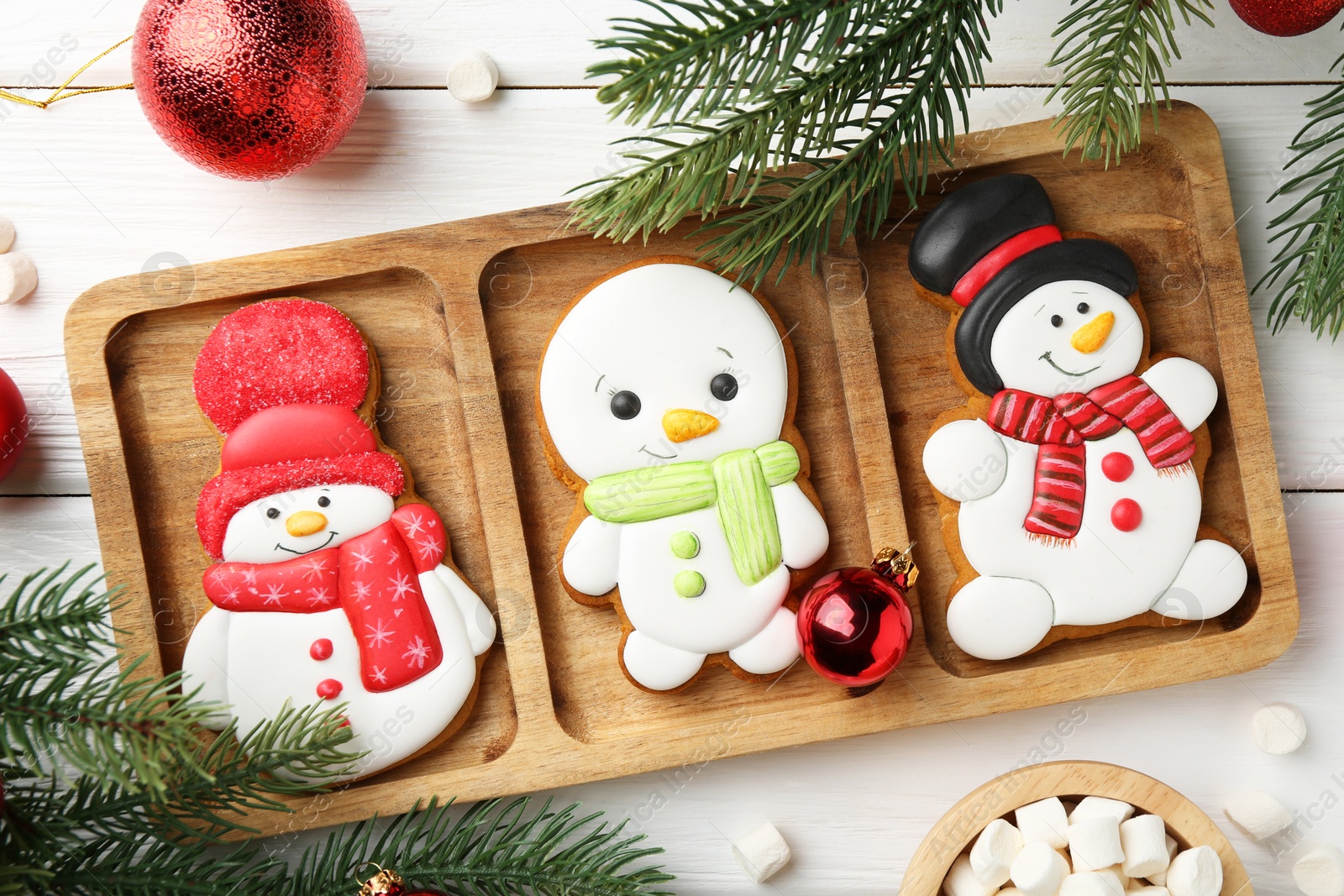 Photo of Delicious cookies in shape of snowmen, marshmallows and Christmas decor on white wooden table, flat lay