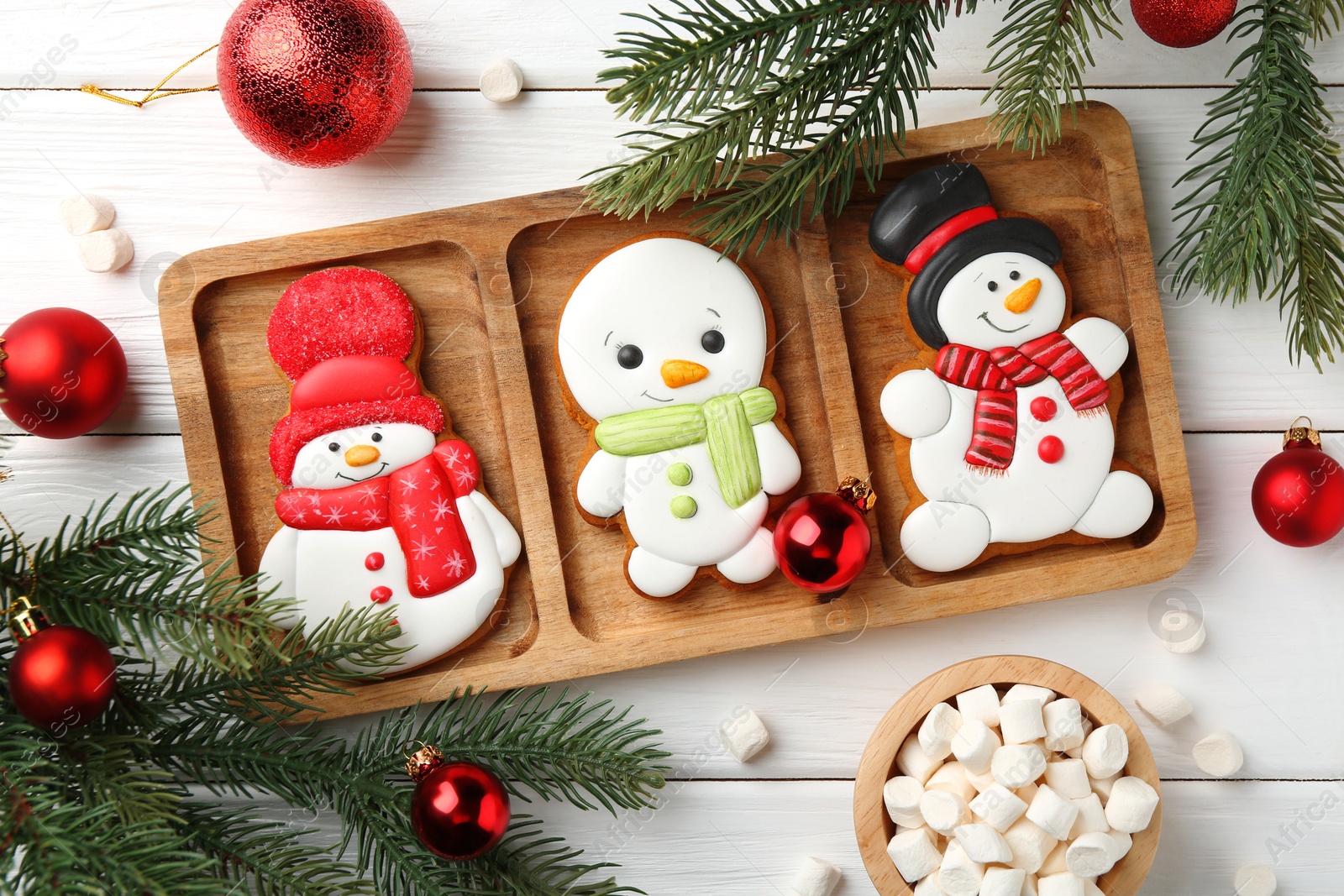 Photo of Delicious cookies in shape of snowmen, marshmallows and Christmas decor on white wooden table, flat lay