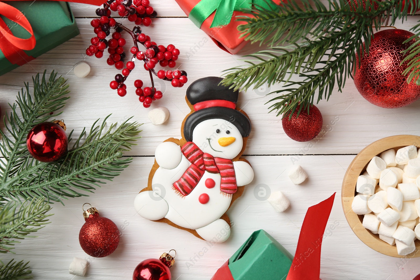 Photo of Delicious cookie in shape of snowman, marshmallows and Christmas decor on white wooden table, flat lay