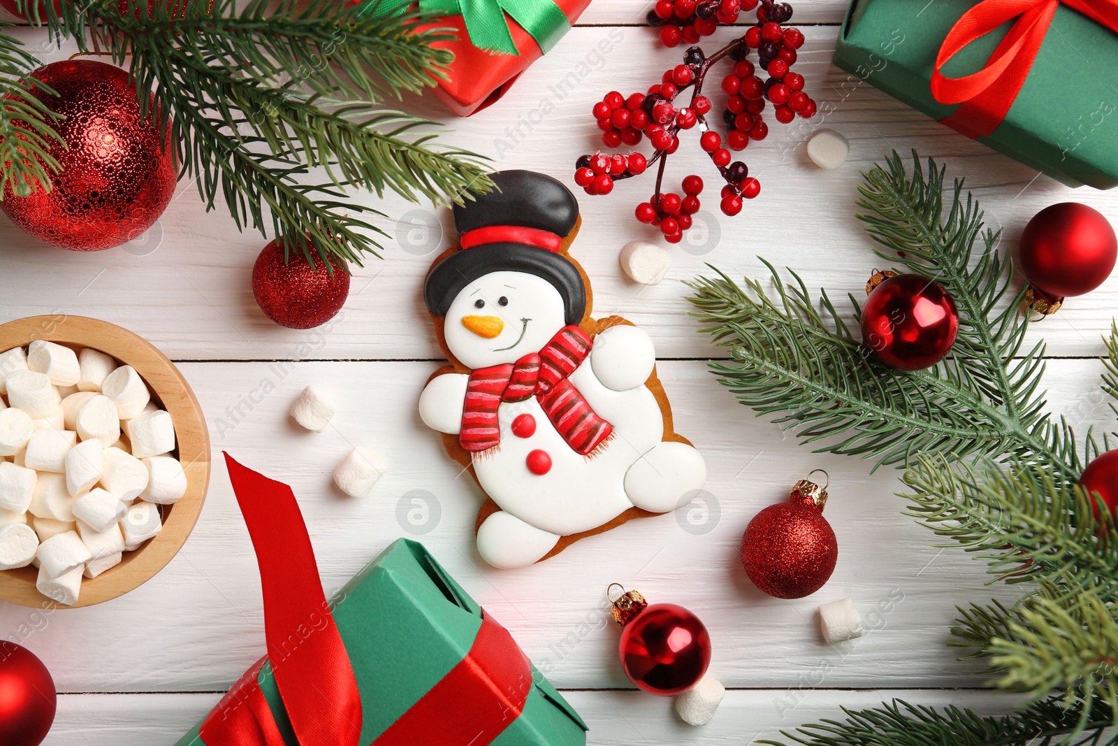 Photo of Delicious cookie in shape of snowman, marshmallows and Christmas decor on white wooden table, flat lay