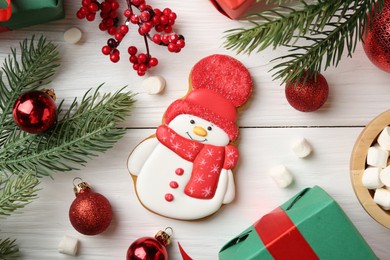 Photo of Delicious cookie in shape of snowman, marshmallows and Christmas decor on white wooden table, flat lay