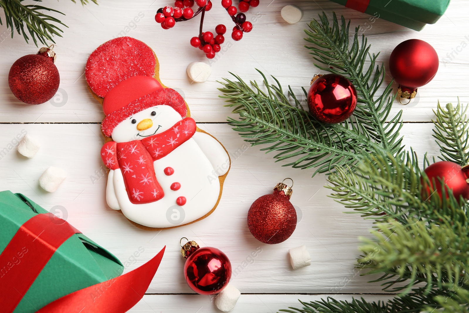 Photo of Delicious cookie in shape of snowman, marshmallows and Christmas decor on white wooden table, flat lay