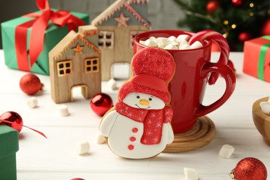 Photo of Delicious cookie in shape of snowman, cup with cocoa and Christmas decor on white wooden table