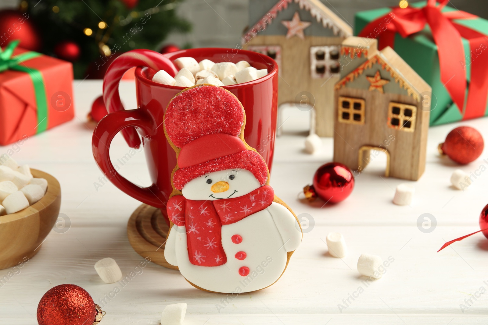 Photo of Delicious cookie in shape of snowman, cup with cocoa and Christmas decor on white wooden table