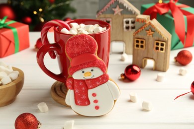 Photo of Delicious cookie in shape of snowman, cup with cocoa and Christmas decor on white wooden table