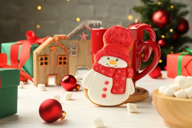 Photo of Delicious cookie in shape of snowman, cup with cocoa and Christmas decor on white wooden table