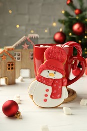 Photo of Delicious cookie in shape of snowman, cup with cocoa and Christmas decor on white wooden table