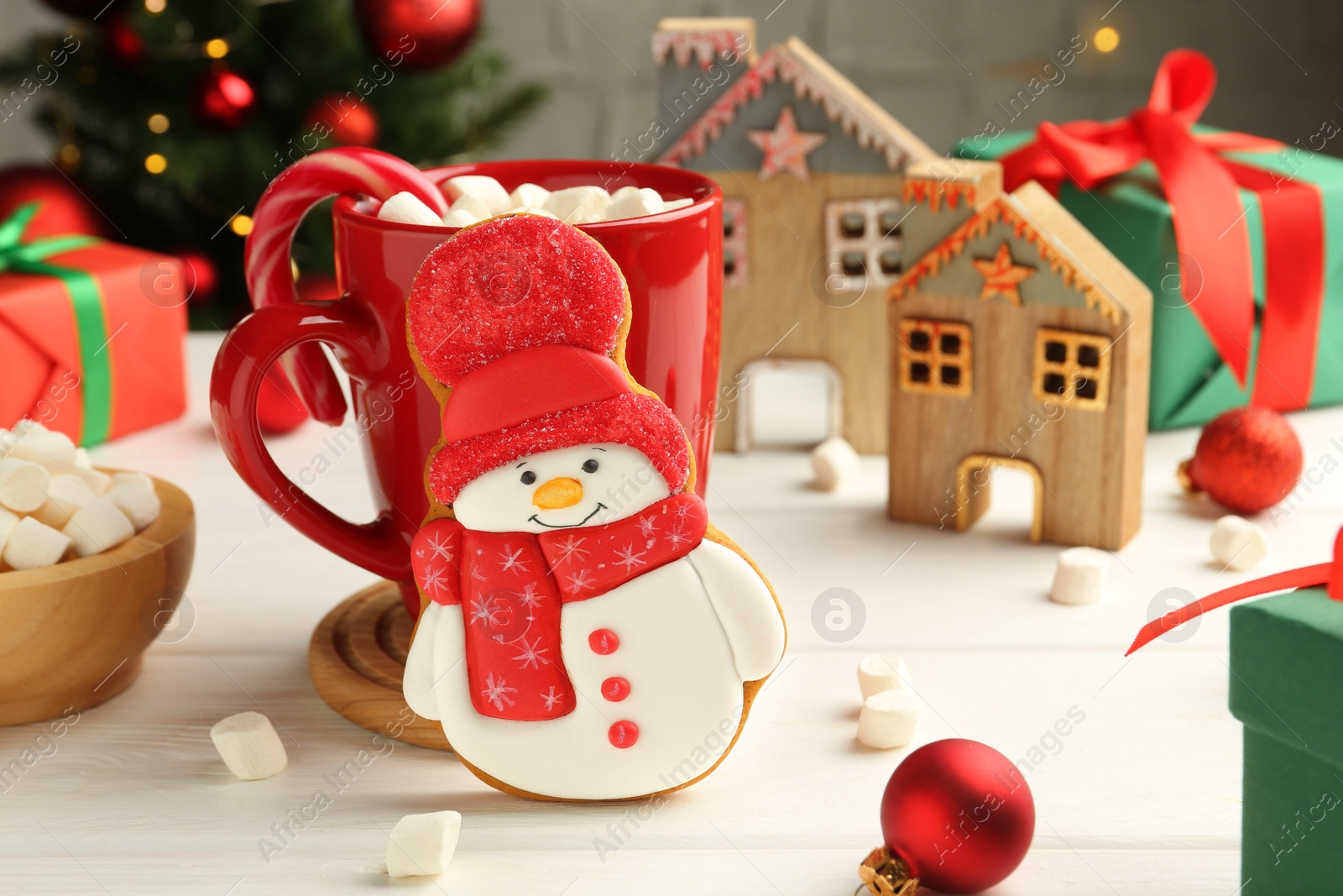 Photo of Delicious cookie in shape of snowman, cup with cocoa and Christmas decor on white wooden table, closeup